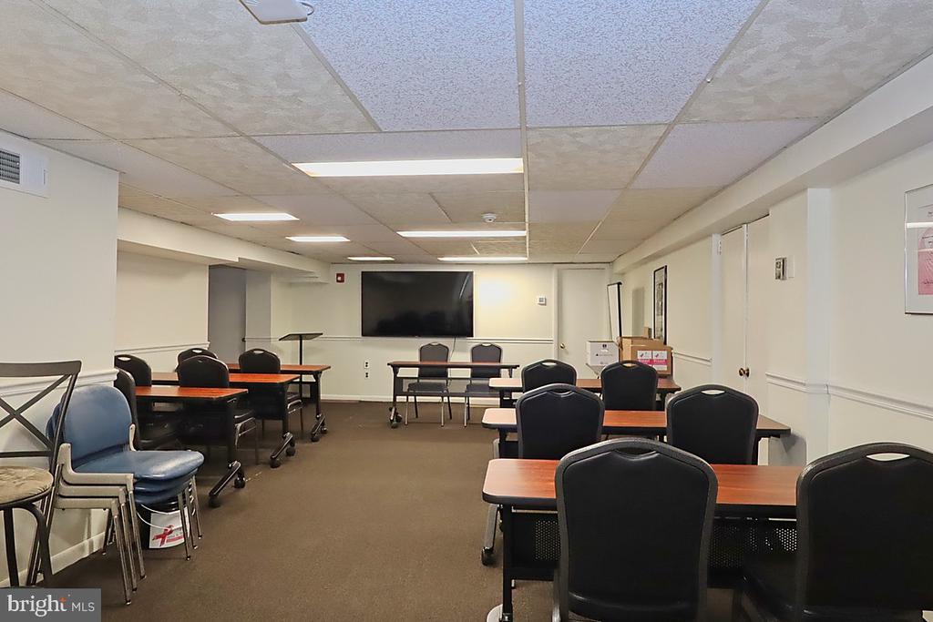 Classroom with rows of tables and chairs facing a large wall-mounted screen.
