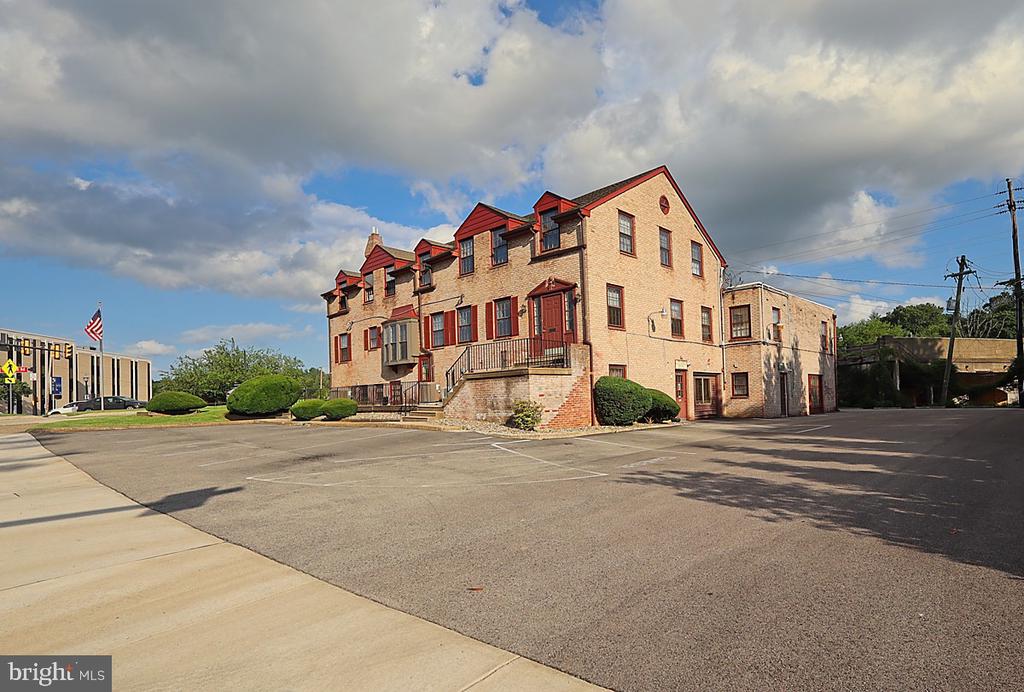 Brick building with red trim and dormers beside a broad paved parking area.