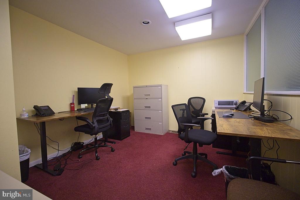 Furnished office with two desks, computer monitors, and red carpet.