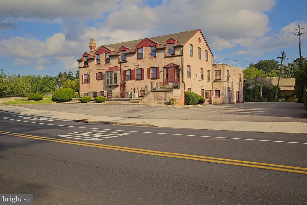Tan brick building with red-trimmed windows and dormers beside a road and parking area.