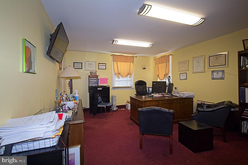 Office with a wooden desk, computer, guest chairs, and framed certificates.