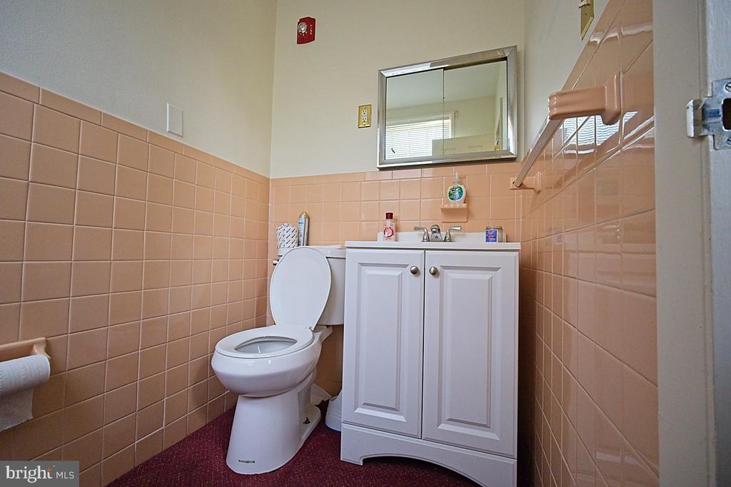 Bathroom with peach-pink tiled walls, white toilet and vanity, and a mirror above the sink.
