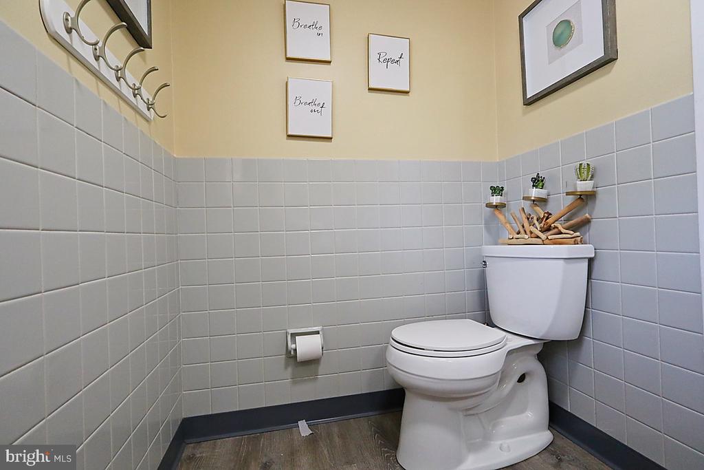 Bathroom with a white toilet, gray tiled walls, and framed breathing-themed prints.