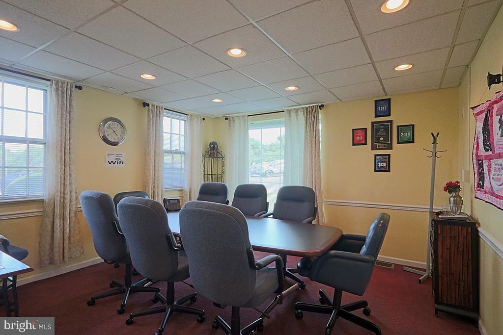 Conference room with a large table, gray rolling chairs, and several curtained windows.