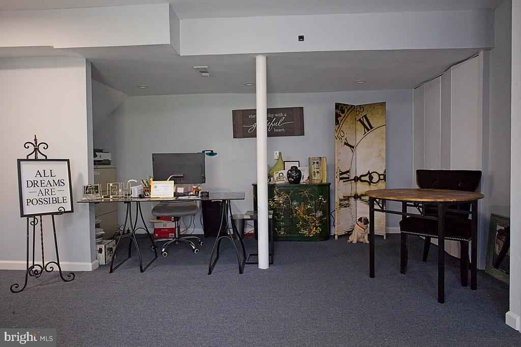 Furnished office with a desk, round table, oversized clock artwork, and small dog.