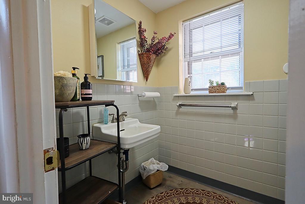 Bathroom with tiled walls, pedestal sink, large mirror, and a bright window with blinds.