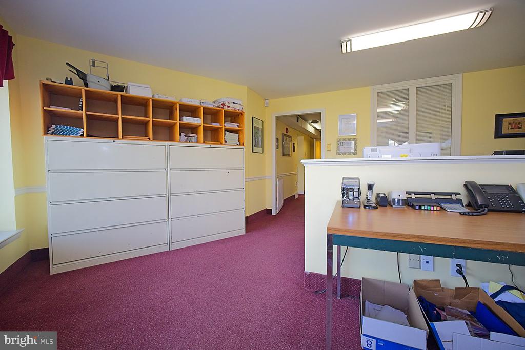 Office reception area with burgundy carpet, filing cabinets, and a desk behind a counter.