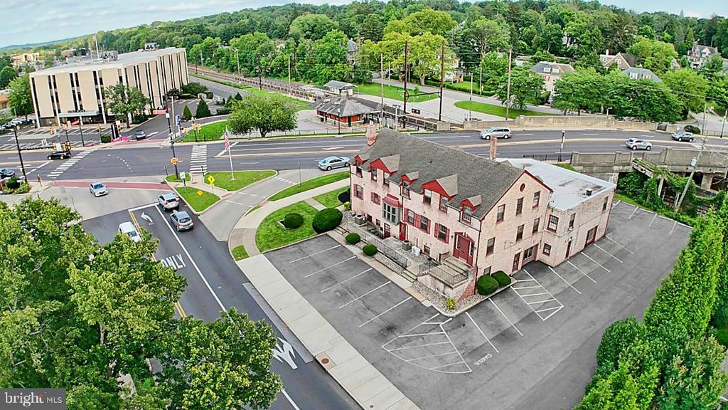 Aerial view of a brick building with red-trimmed windows beside a large parking lot and busy intersection.