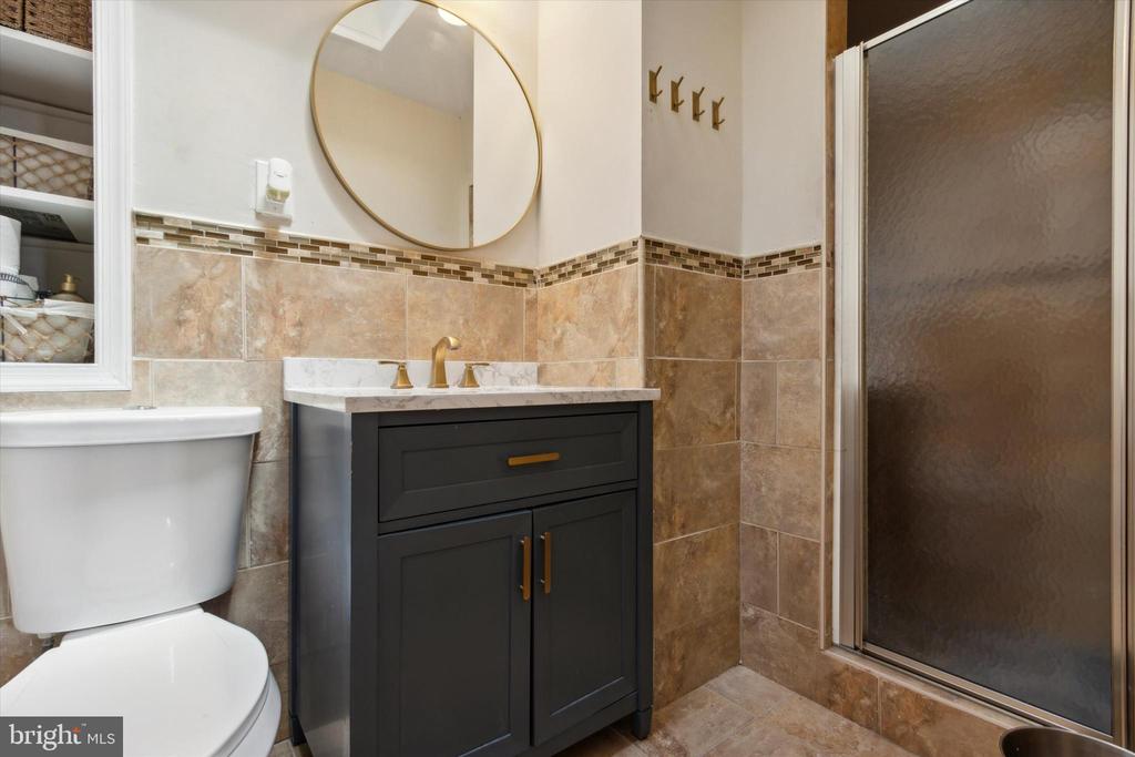 Bathroom with a dark vanity, round mirror, tan tile, and frosted-glass shower.