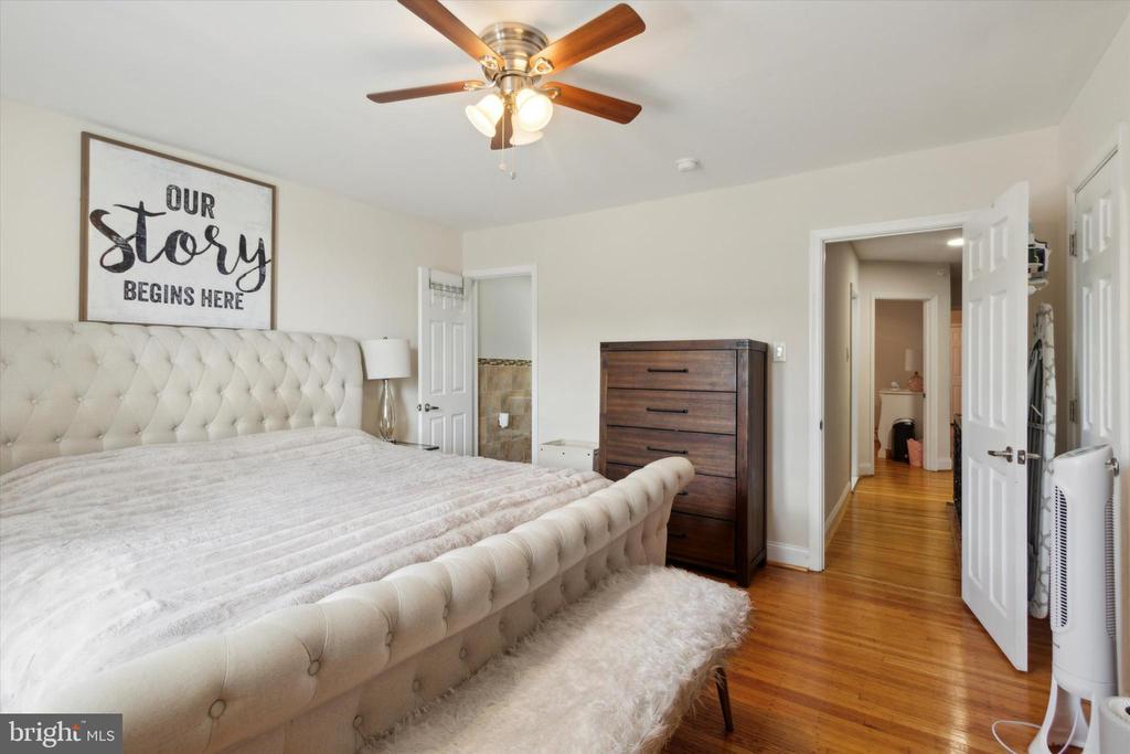 Furnished bedroom with a tufted bed, dark wood dresser, ceiling fan, and hardwood floors.