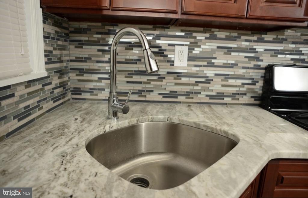 Kitchen sink with a tall curved faucet, marble-pattern countertop, and gray mosaic tile backsplash.