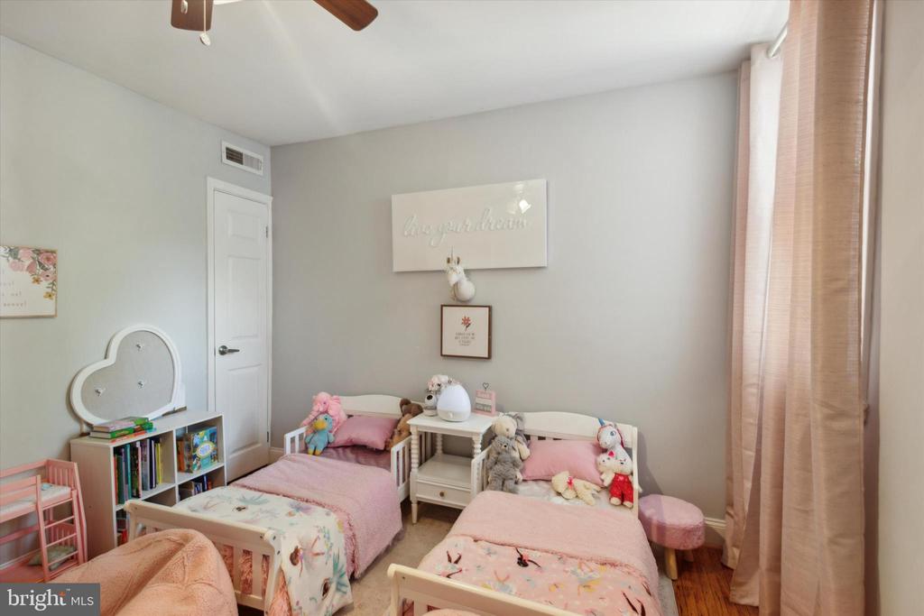 Children’s bedroom with two pink-covered twin beds, plush toys, and pink curtains.