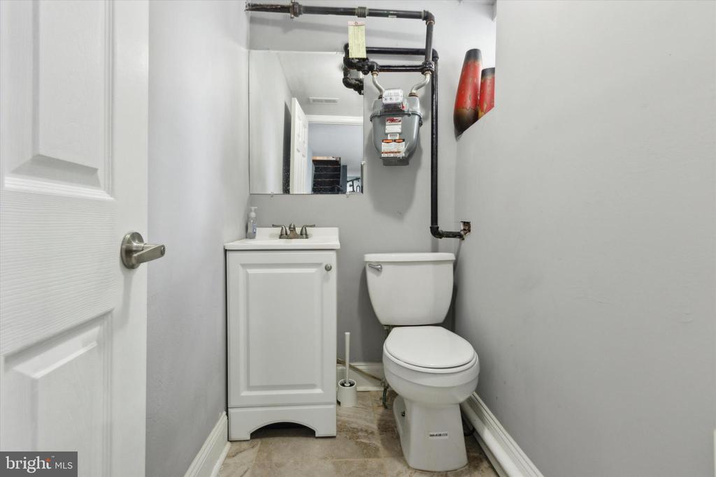 Half bathroom with a white toilet, compact vanity, and exposed gas meter and pipes.