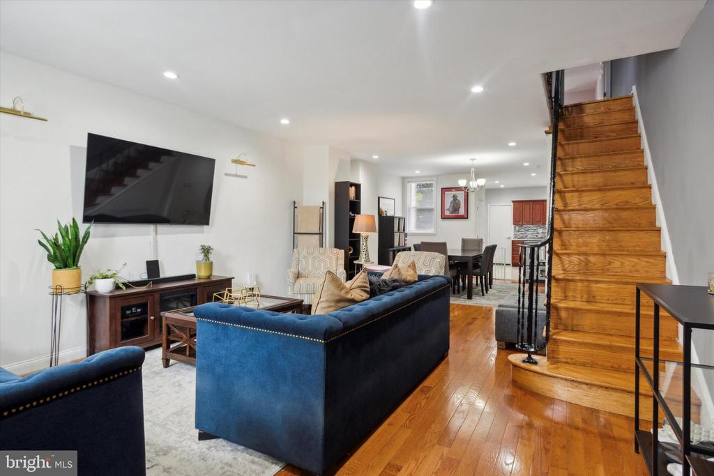 Open living room with blue sofas, hardwood floors, and a staircase beside the dining area.