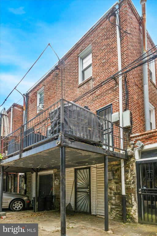 Red-brick rowhouse with a raised metal balcony and covered parking beneath.