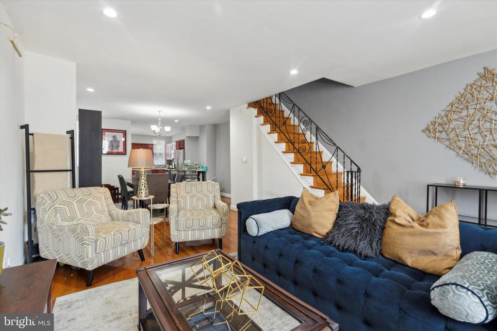 Living room with a blue tufted sofa, patterned armchairs, and a decorative staircase.