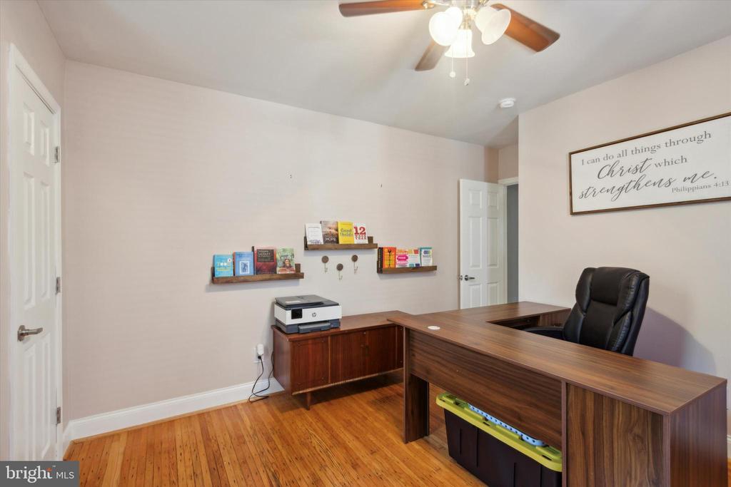 Home office with an L-shaped wood desk, black chair, hardwood floors, and wall-mounted book shelves.