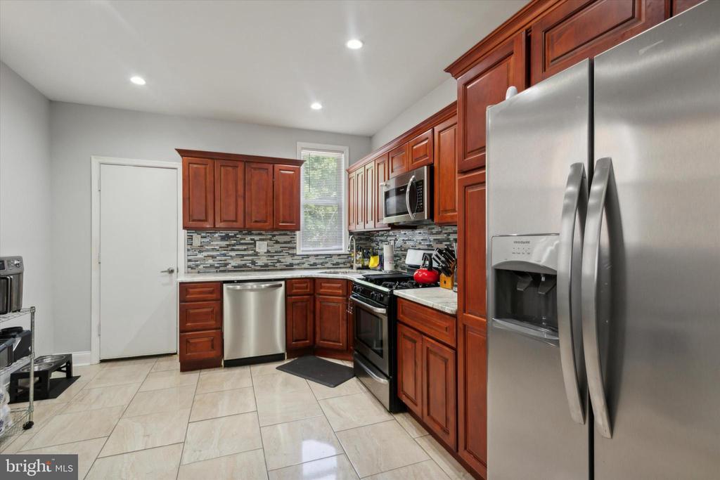 Kitchen with reddish wood cabinets, a multicolored tile backsplash, and stainless steel appliances.