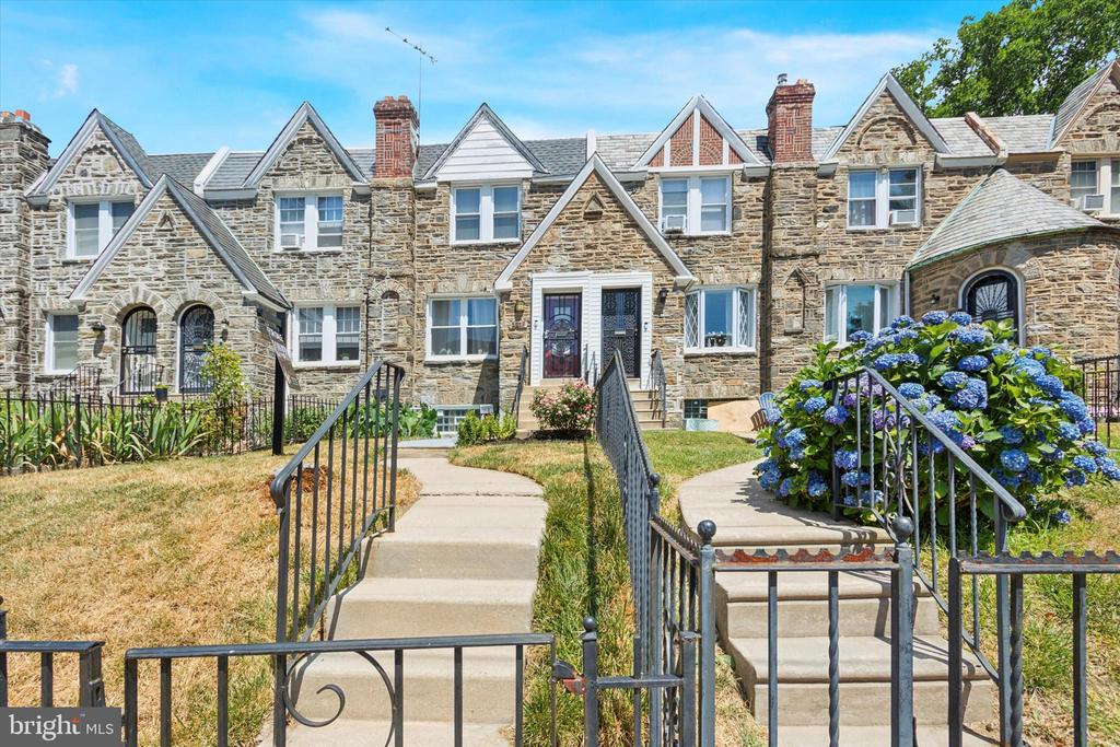 Stone rowhomes with steep gables, front steps, black railings, and a blue hydrangea.
