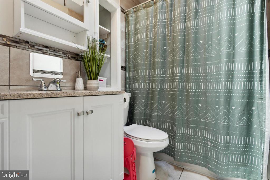 Bathroom with a white vanity, tiled backsplash, and patterned teal shower curtain.
