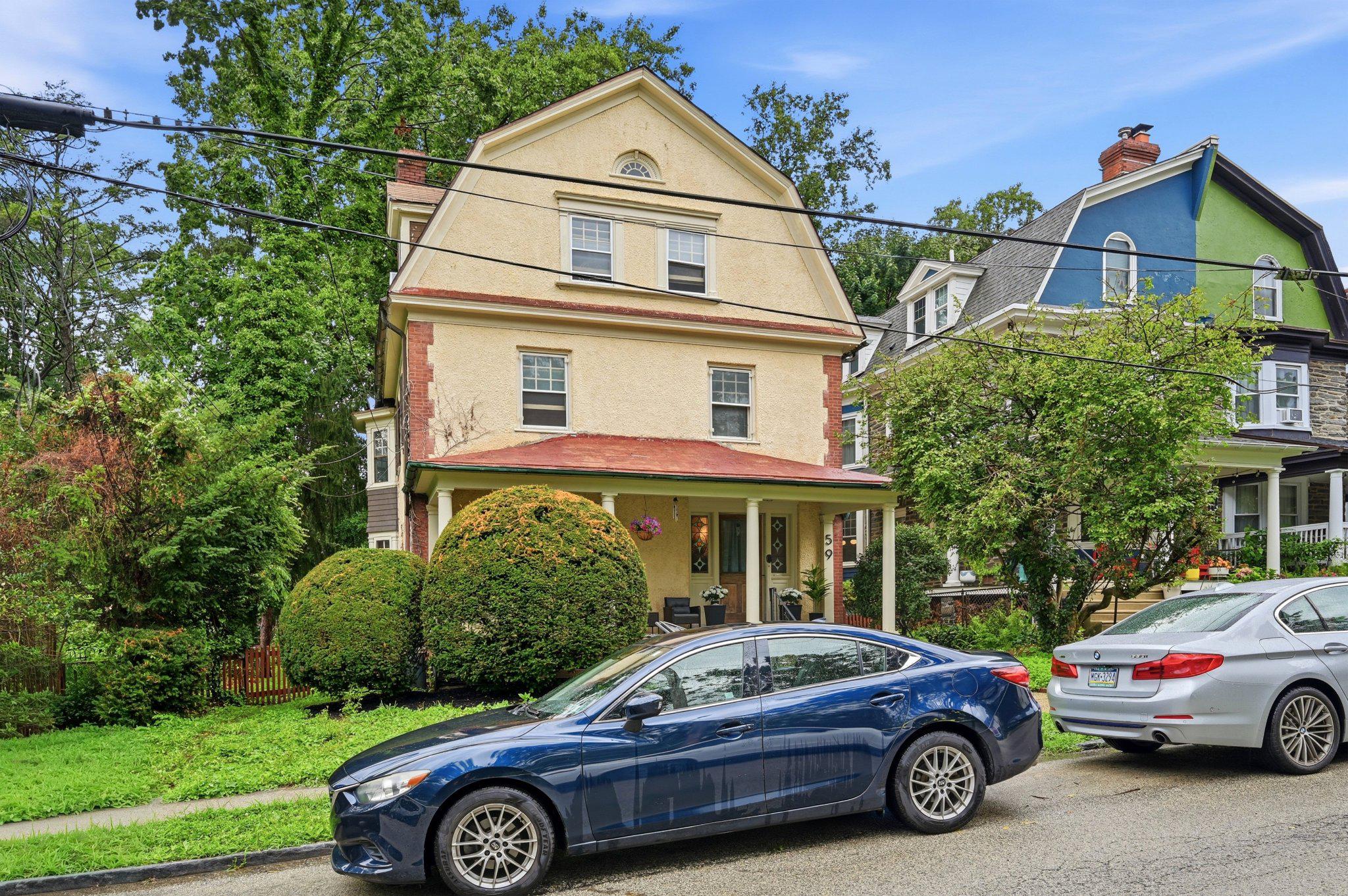 Beige three-story house with a covered porch, brick accents, and rounded front shrubs.