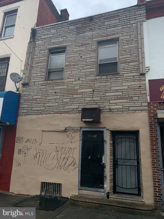 Philadelphia rowhouse with a gray stone upper facade, graffiti on the lower wall, and two ground-level doors.
