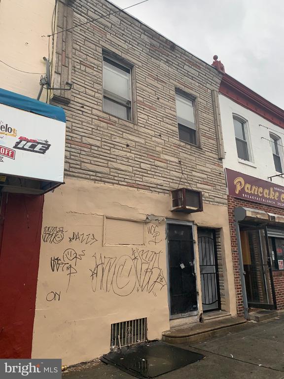 Two-story masonry Philadelphia building with a gated entrance, graffiti, and neighboring pancake restaurant.