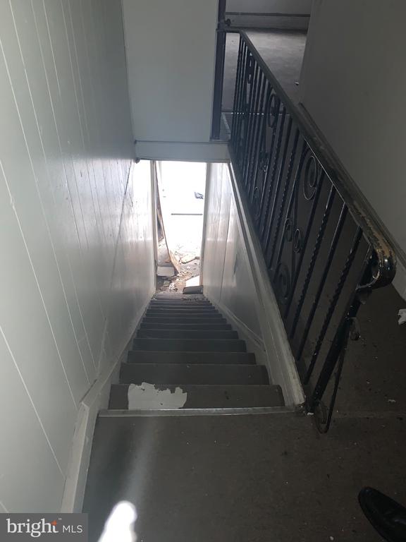Interior stairwell with a black iron railing, chipped paint, and debris near the lower doorway.