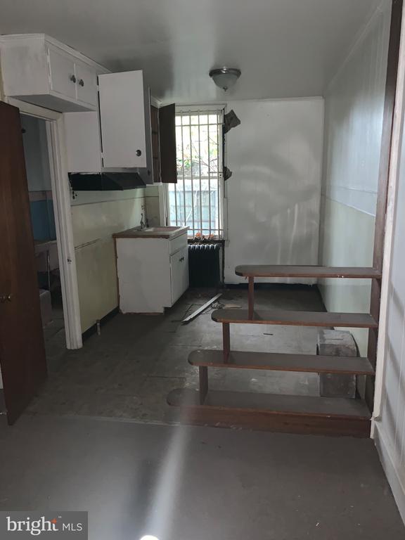 Vacant kitchen with white cabinets and sink beside open-riser wooden stairs.