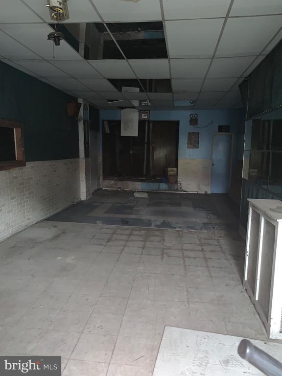 Vacant commercial interior with a tiled floor, right-side counter, and missing ceiling panels.