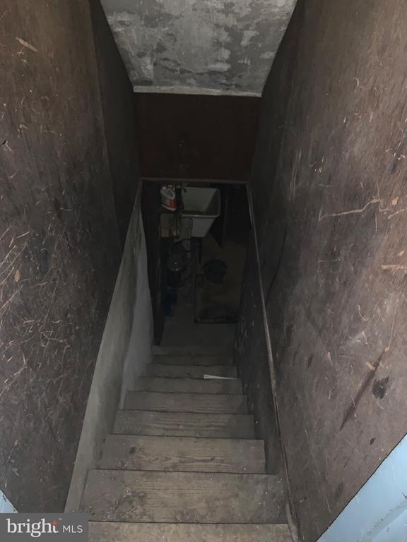 Narrow unfinished basement staircase descending toward a toilet.