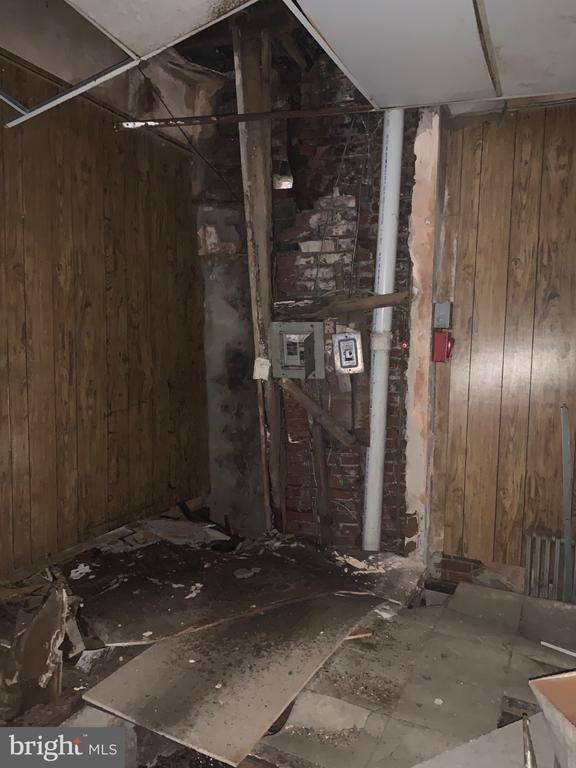 Unfinished interior with exposed brick, utility pipes, damaged ceiling, and debris-covered floor.