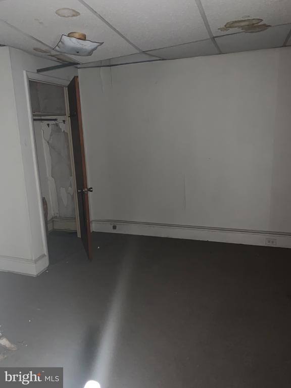 Empty room with dark flooring, an open closet, and damaged ceiling tiles.