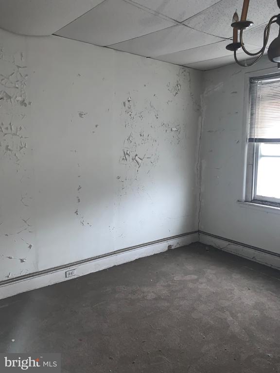 Vacant room with peeling walls, a bare stained floor, and a window with blinds.