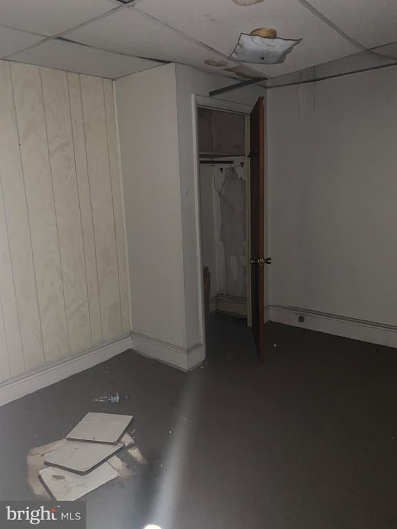 Empty room with an open closet, debris on the floor, and damaged ceiling tiles.