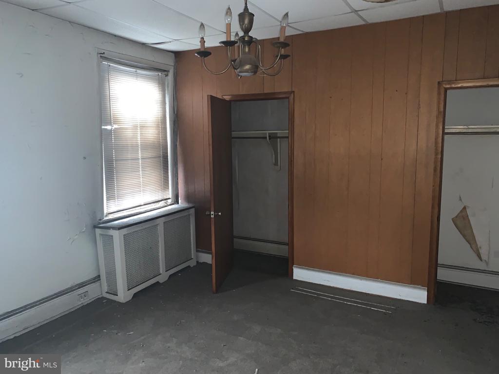 Empty room with wood-paneled walls, an open closet, and a window with blinds.