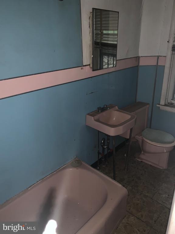 Vacant bathroom with a pink bathtub, sink, and toilet against blue walls.