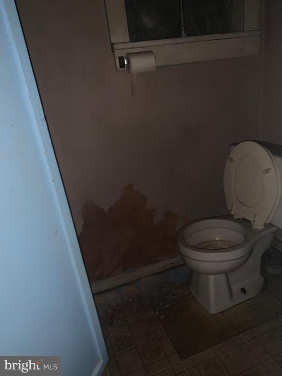 Bathroom with a toilet, damaged wall plaster, and a worn tiled floor.