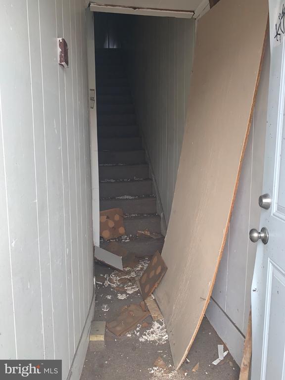 Damaged stairwell with debris on the steps and a detached panel leaning against the wall.