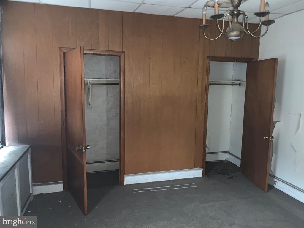 Empty bedroom with wood-paneled walls, gray carpet, chandelier, and two open closets.