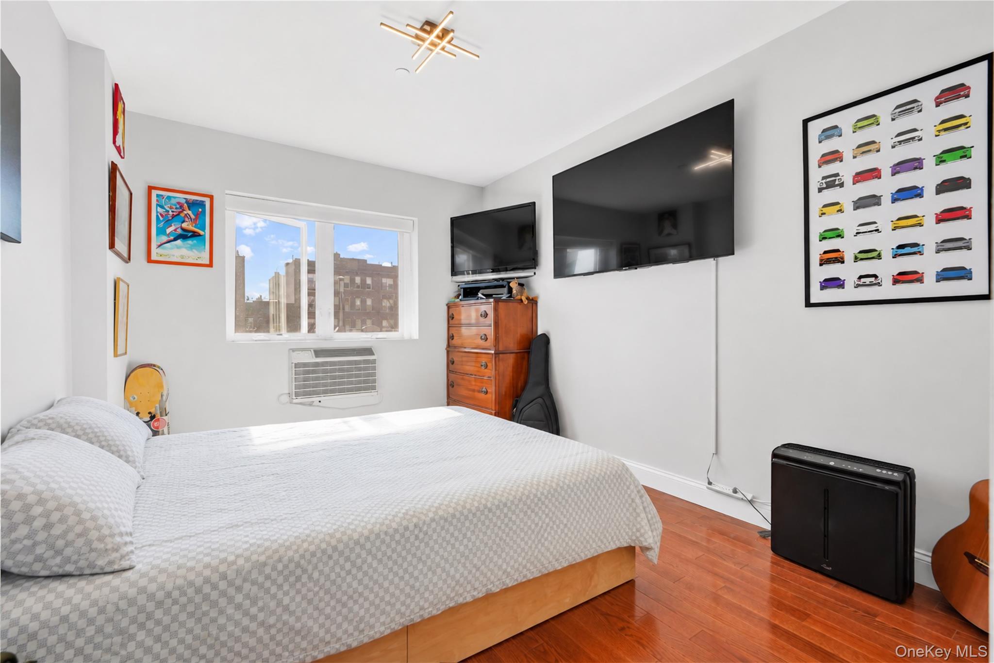 Bedroom with hardwood floors, two wall-mounted televisions, and framed colorful car artwork.