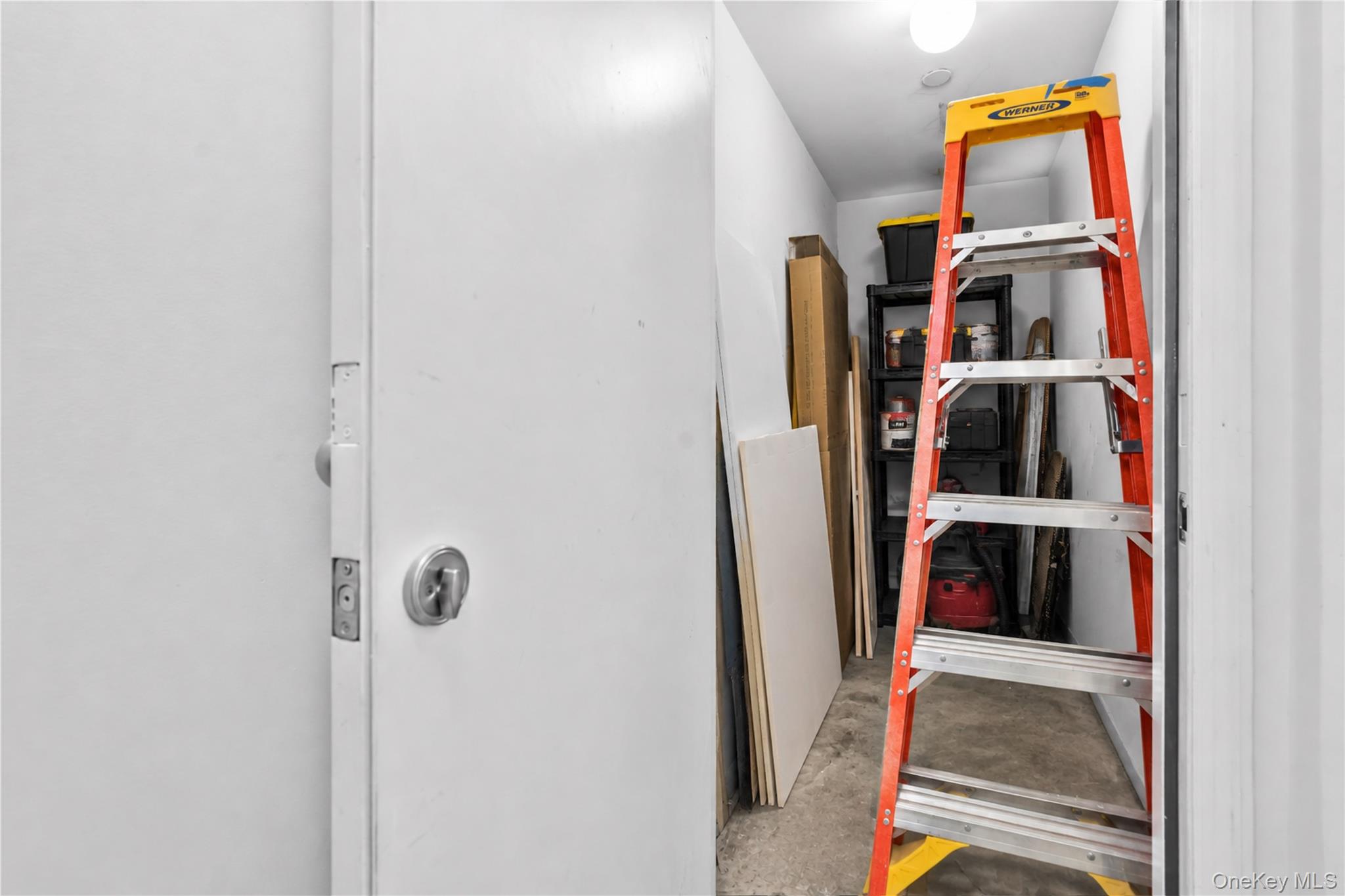 Storage room with a red and yellow ladder, shelves, tools, and building materials.