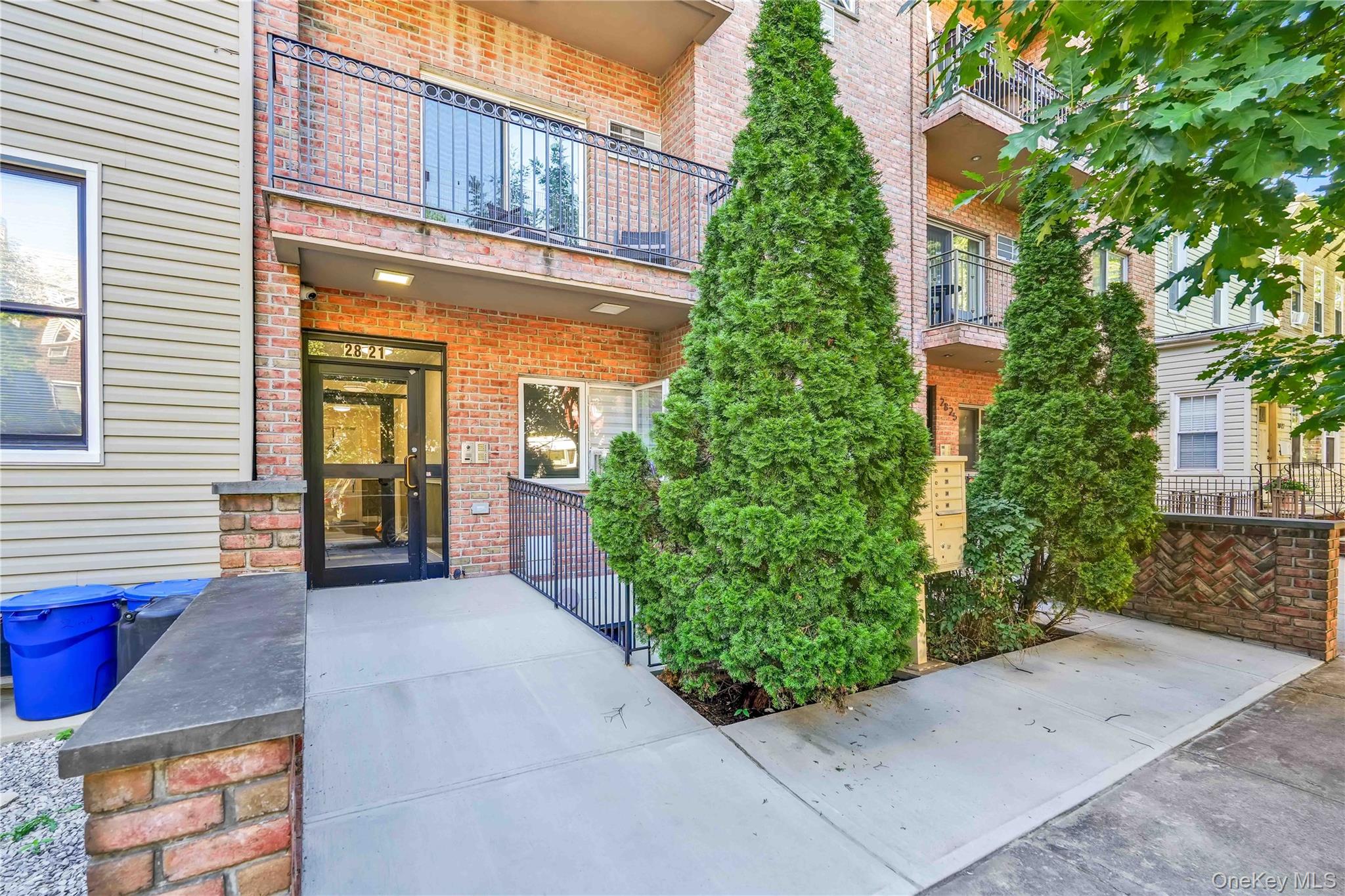 Brick apartment building entrance marked 2821, with balconies and tall evergreen shrubs.