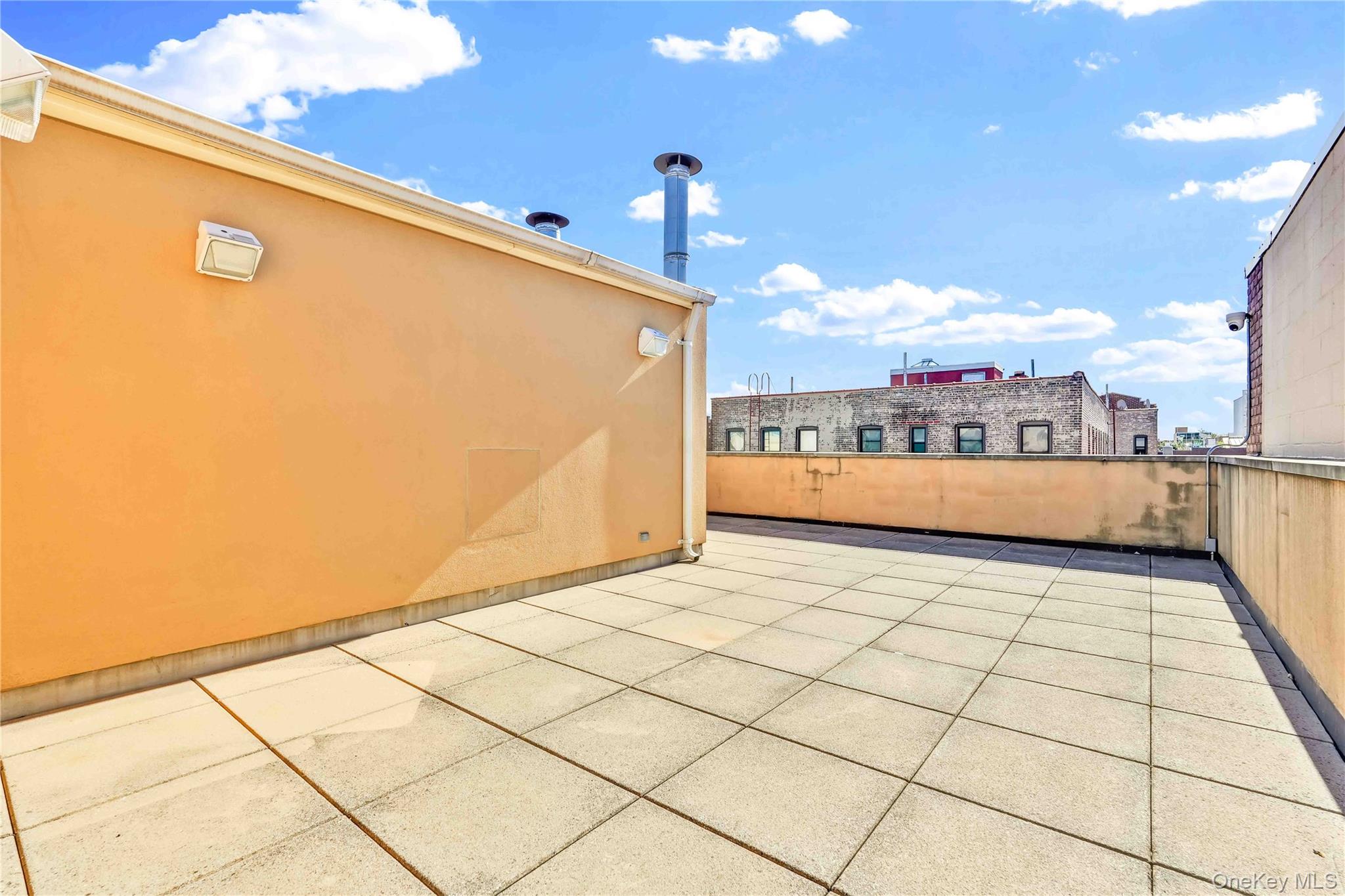 Rooftop terrace with tiled flooring and orange walls overlooking neighboring buildings.
