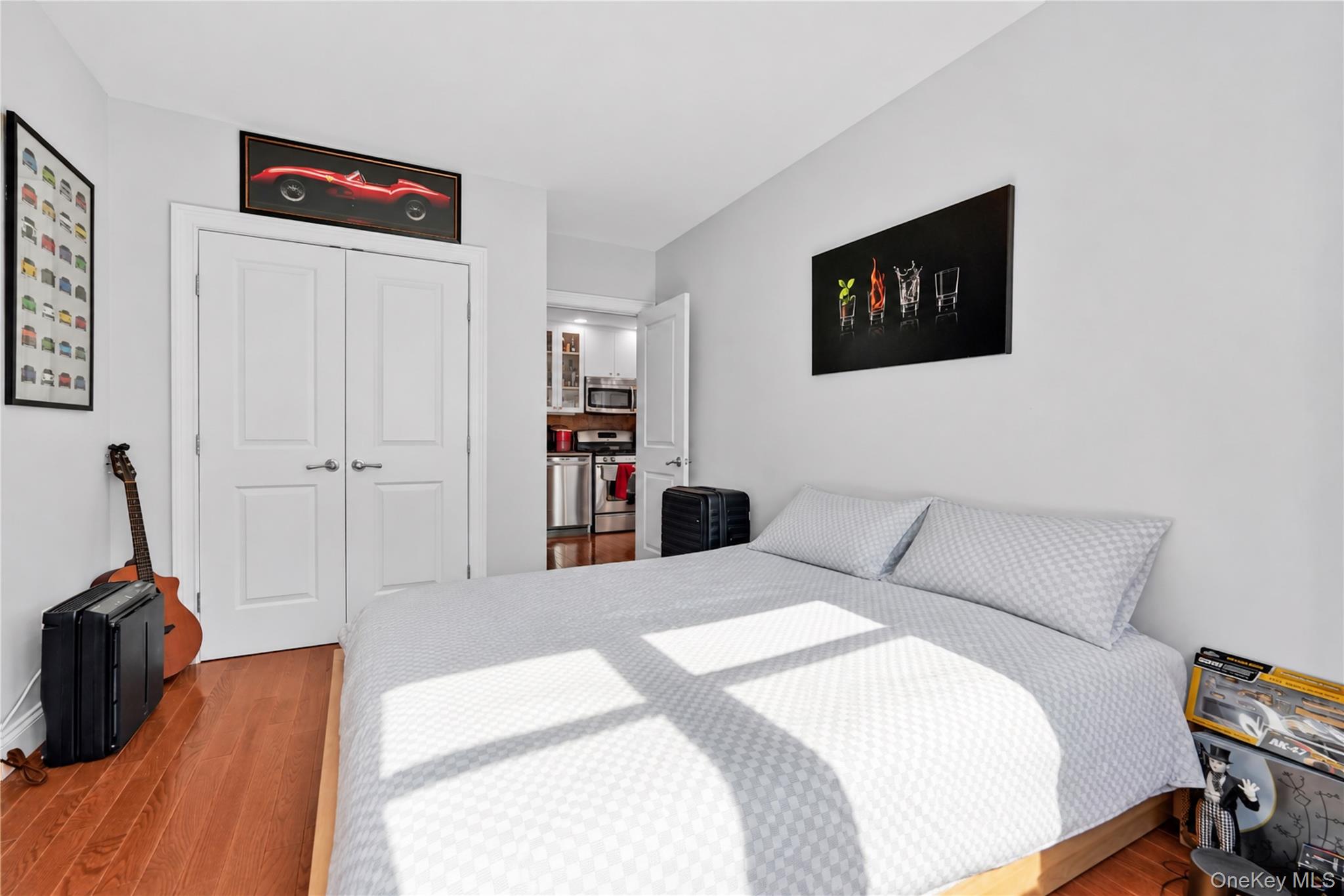 Bedroom with a large gray-patterned bed, warm wood floors, and bright sunlight across the bedding.