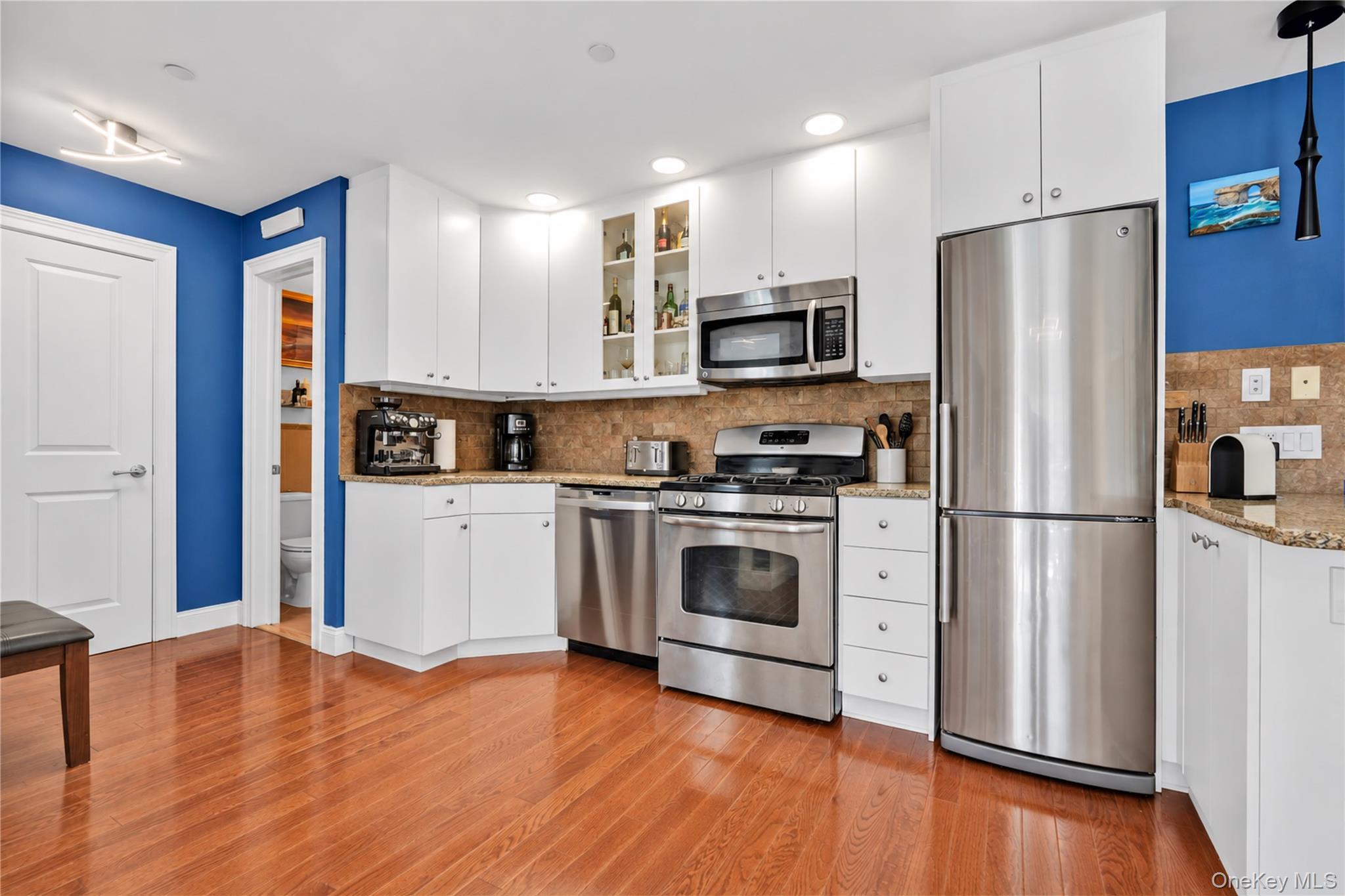 Kitchen with white cabinets, stainless steel appliances, blue walls, and hardwood floors.