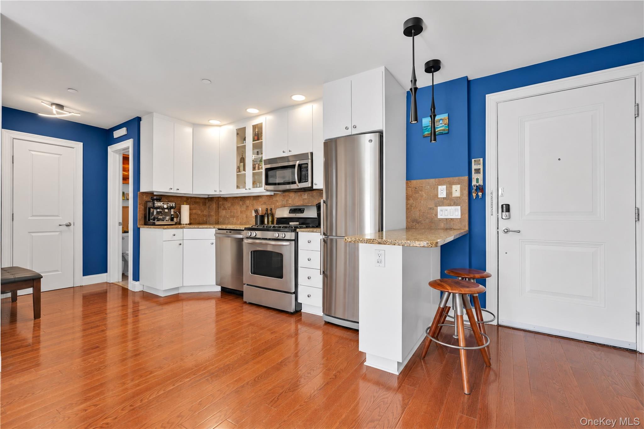 Apartment kitchen with stainless steel appliances, white cabinets, blue walls, and a peninsula with two stools.