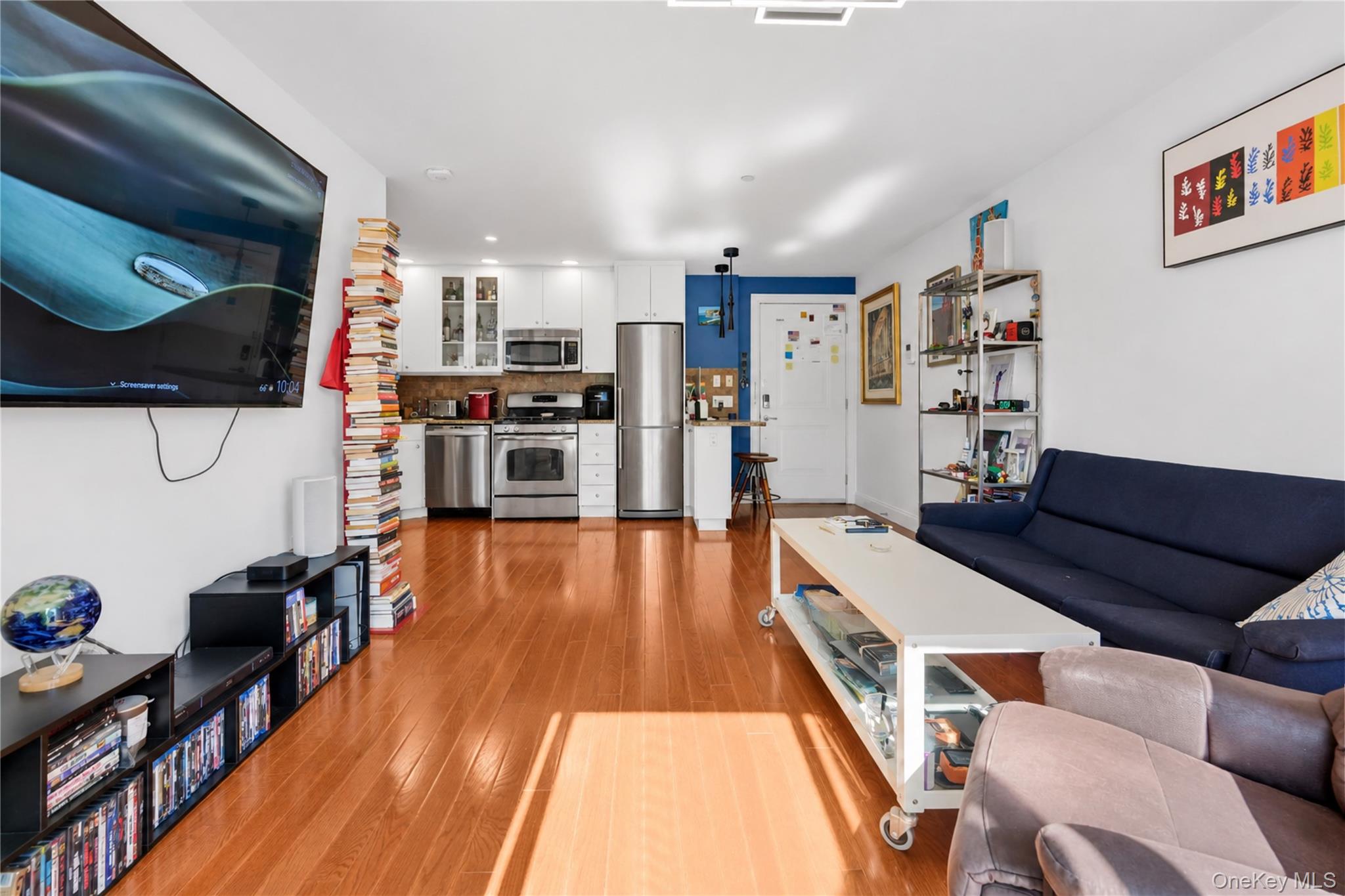 Open-plan living room and kitchen with polished wood floors, stainless steel appliances, and a navy sofa.