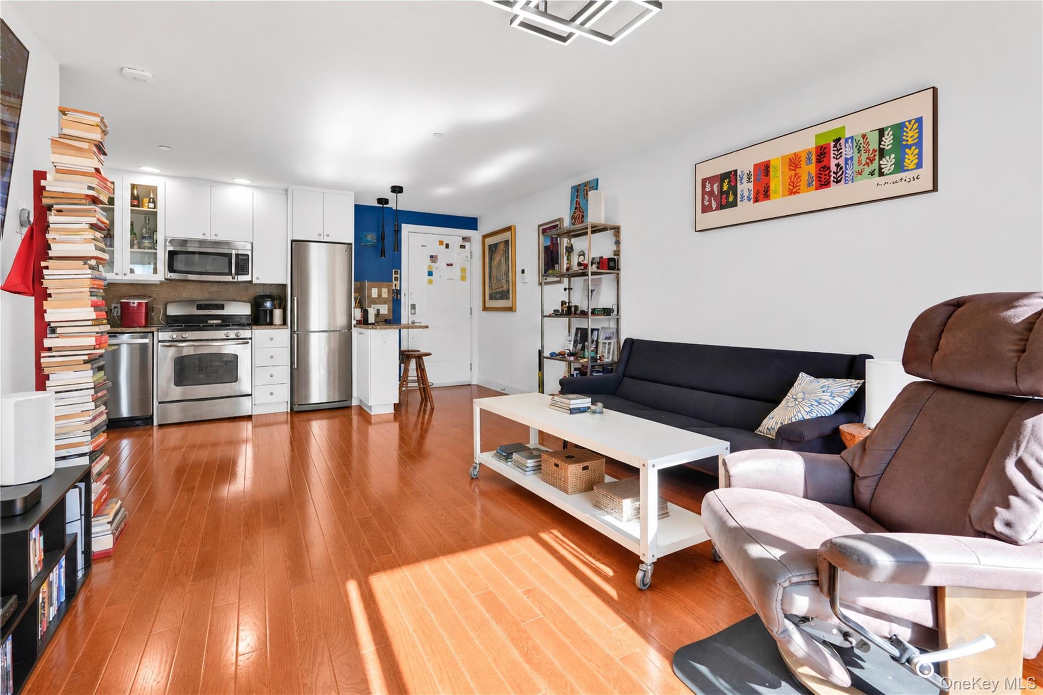 Open-plan living room and kitchen with stainless steel appliances, wood floors, dark sofa, and brown recliner.