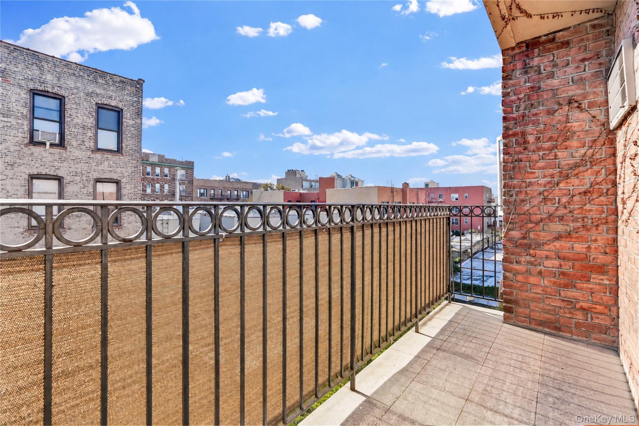 Apartment balcony with tiled floor and metal railing overlooking neighboring brick buildings.
